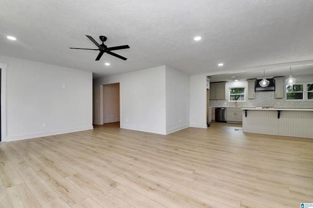 unfurnished living room featuring a textured ceiling, light hardwood / wood-style flooring, ceiling fan, and sink