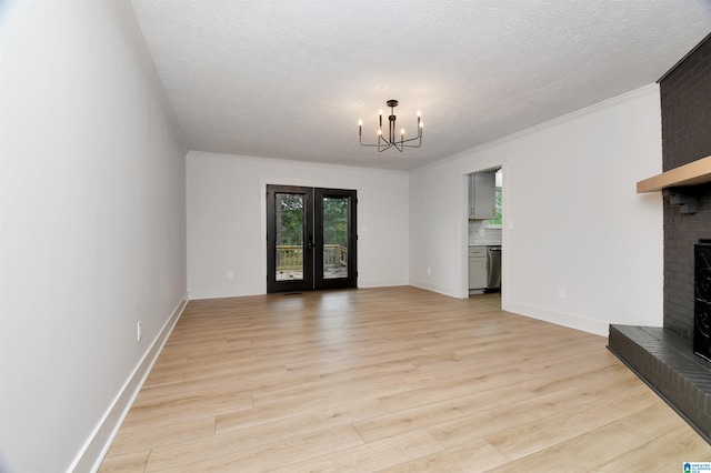 unfurnished living room featuring an inviting chandelier, crown molding, a brick fireplace, light wood-type flooring, and a textured ceiling