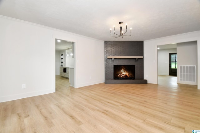 unfurnished living room featuring a textured ceiling, an inviting chandelier, a fireplace, light hardwood / wood-style floors, and ornamental molding