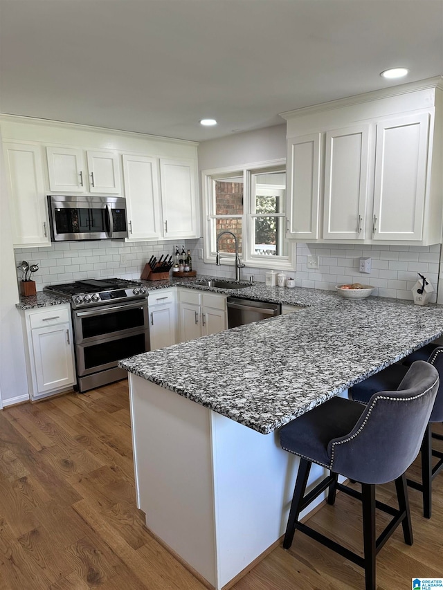 kitchen with stainless steel appliances, sink, hardwood / wood-style flooring, dark stone countertops, and white cabinets