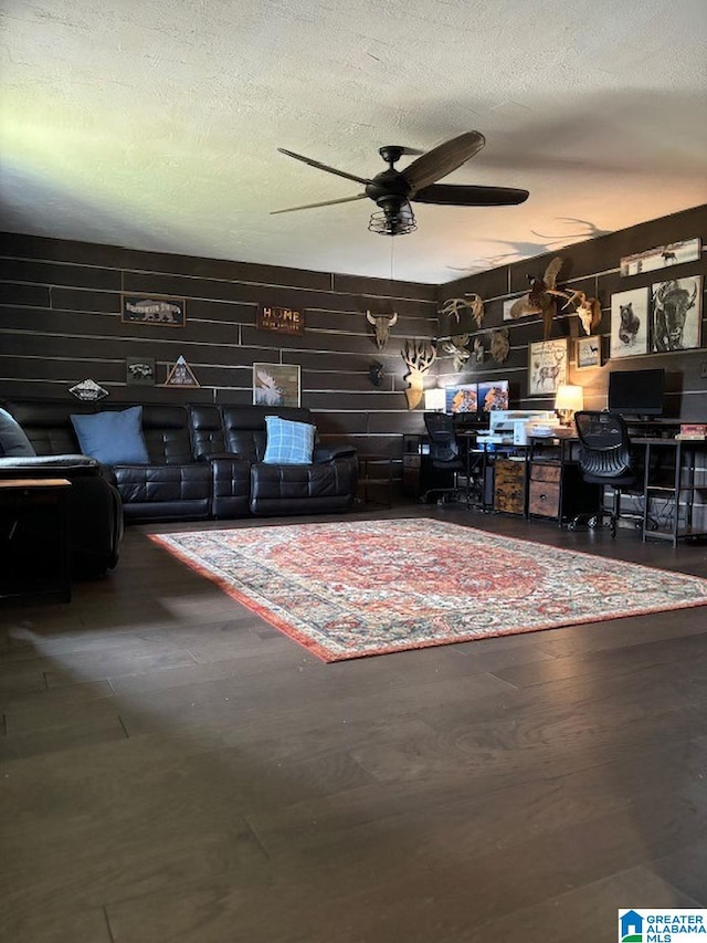 living room with wood walls, ceiling fan, and a textured ceiling