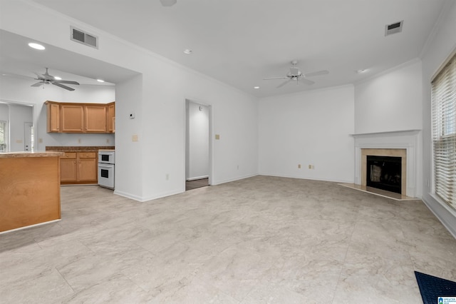 unfurnished living room featuring crown molding, ceiling fan, and a tiled fireplace