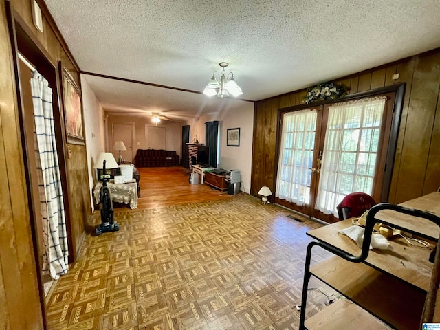 living room with a textured ceiling, wood walls, a notable chandelier, french doors, and parquet flooring