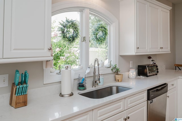 kitchen with light stone countertops, dishwasher, white cabinetry, and sink