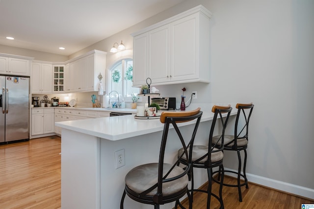 kitchen featuring stainless steel fridge, light hardwood / wood-style floors, kitchen peninsula, and a breakfast bar