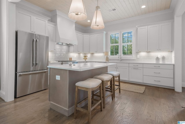 kitchen with white cabinetry, stainless steel appliances, a breakfast bar area, a kitchen island, and custom range hood