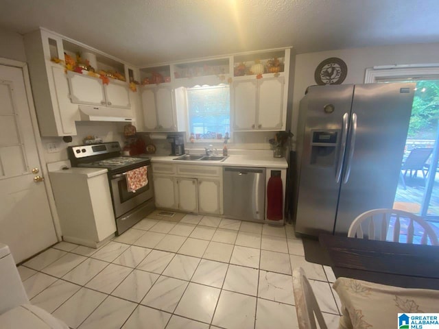 kitchen with white cabinets, appliances with stainless steel finishes, sink, light tile patterned flooring, and a textured ceiling