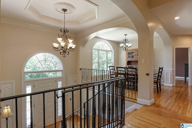 hall featuring crown molding, a tray ceiling, a chandelier, and light hardwood / wood-style floors