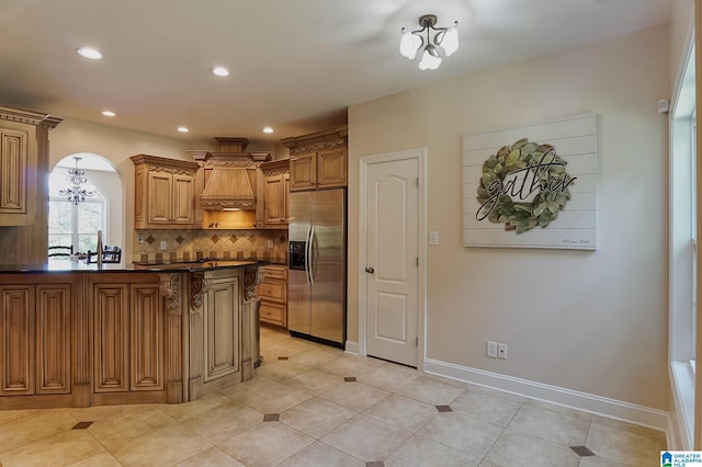 kitchen with built in fridge, light tile patterned floors, premium range hood, tasteful backsplash, and a chandelier