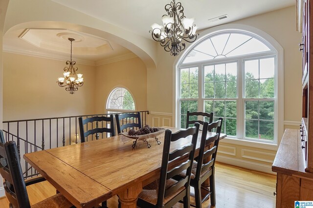 dining room with crown molding, a raised ceiling, an inviting chandelier, and light wood-type flooring