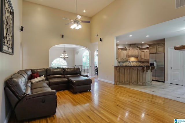 living room featuring ceiling fan with notable chandelier, high vaulted ceiling, sink, and light hardwood / wood-style floors