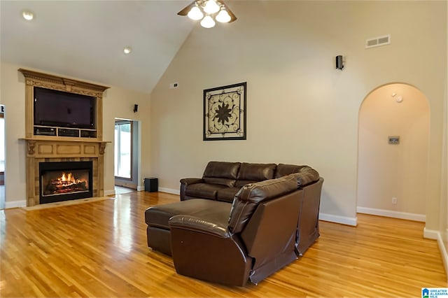 living room with high vaulted ceiling, ceiling fan, a fireplace, and light hardwood / wood-style floors