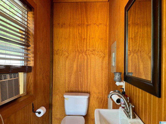 bathroom with a healthy amount of sunlight, toilet, wood walls, and sink