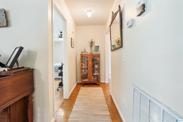 hall featuring parquet floors, visible vents, baseboards, and a textured ceiling