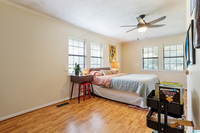 bedroom with crown molding, visible vents, a textured ceiling, and light wood-style floors