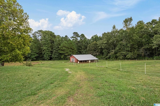 view of yard with an outdoor structure, a wooded view, a rural view, an outbuilding, and fence