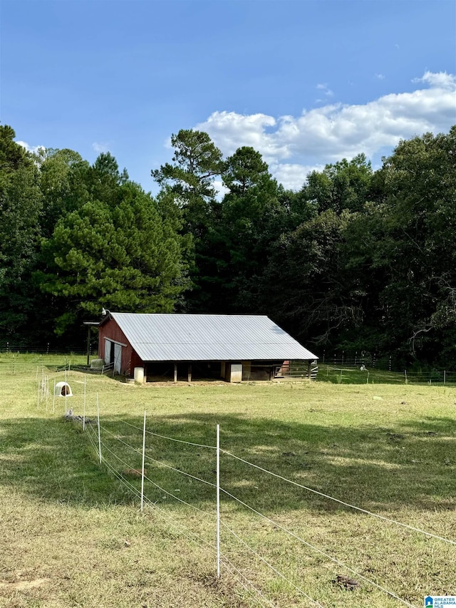 view of pole building with a rural view, a yard, a forest view, and fence