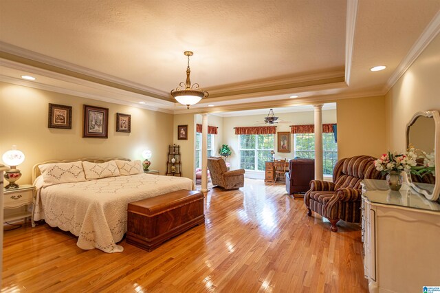 bedroom with a textured ceiling, light hardwood / wood-style flooring, ornate columns, a raised ceiling, and ornamental molding