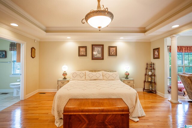 bedroom featuring a tray ceiling, ornamental molding, light hardwood / wood-style floors, and ornate columns