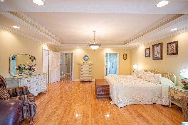 bedroom with a raised ceiling, connected bathroom, crown molding, and light hardwood / wood-style flooring