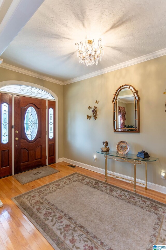 foyer featuring light wood-type flooring, crown molding, a notable chandelier, and a textured ceiling