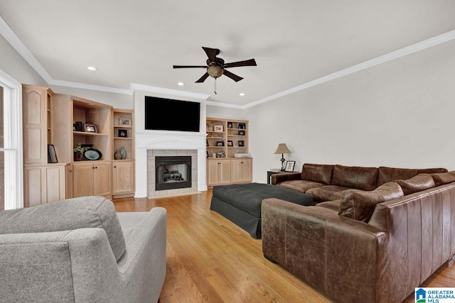 living room with light hardwood / wood-style flooring, ceiling fan, ornamental molding, and a tile fireplace