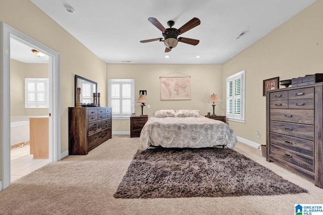 bedroom with multiple windows, light colored carpet, connected bathroom, and ceiling fan