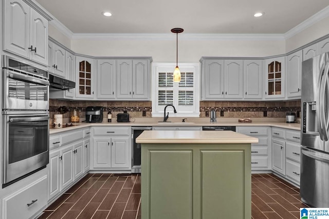 kitchen with pendant lighting, crown molding, stainless steel appliances, a center island, and sink