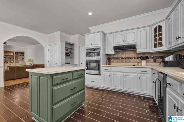 kitchen featuring white cabinets, crown molding, dark wood-type flooring, decorative backsplash, and double oven