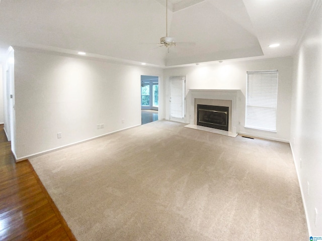 unfurnished living room with a tray ceiling, a premium fireplace, ceiling fan, and carpet flooring