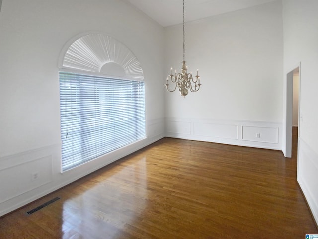 spare room with dark hardwood / wood-style floors, a chandelier, and a towering ceiling