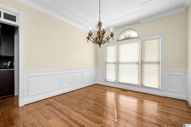 unfurnished dining area featuring ornamental molding, hardwood / wood-style flooring, and a notable chandelier