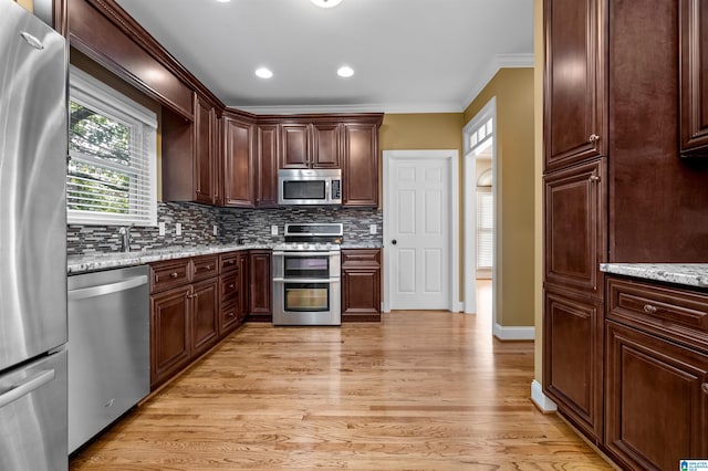 kitchen with crown molding, light wood-type flooring, appliances with stainless steel finishes, light stone countertops, and tasteful backsplash