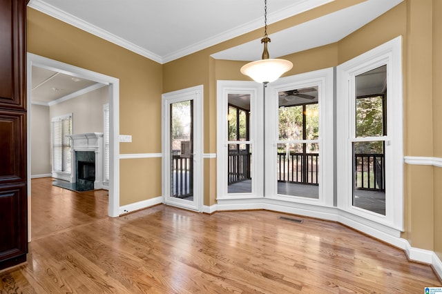 doorway with a wealth of natural light, light hardwood / wood-style floors, crown molding, and a premium fireplace