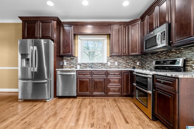 kitchen with stainless steel appliances, ornamental molding, decorative backsplash, light stone counters, and light wood-type flooring