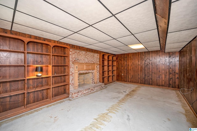 basement with a paneled ceiling, wood walls, and a brick fireplace