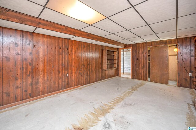 basement featuring wooden walls and a drop ceiling