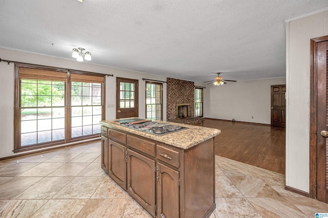 kitchen featuring a textured ceiling, light hardwood / wood-style flooring, a brick fireplace, a center island, and ceiling fan