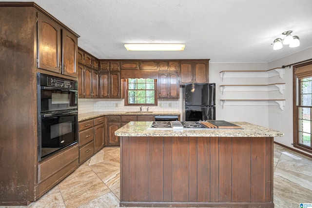 kitchen featuring black appliances, light stone counters, a center island, and decorative backsplash