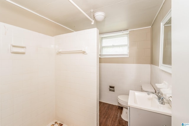 bathroom with toilet, vanity, a tile shower, tile walls, and hardwood / wood-style flooring