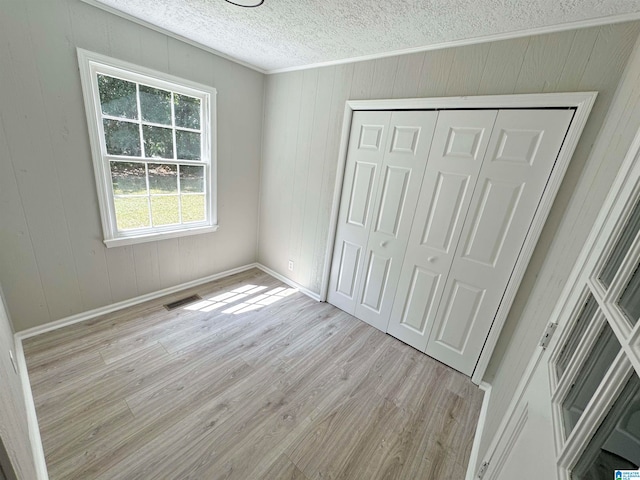 unfurnished bedroom with a closet, light hardwood / wood-style floors, wood walls, and a textured ceiling