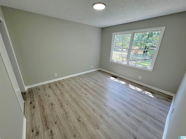 spare room with light wood-type flooring and a textured ceiling