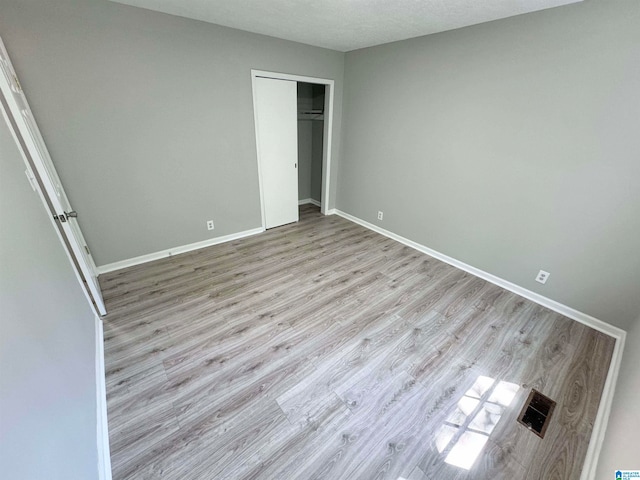 unfurnished bedroom with light wood-type flooring, a textured ceiling, and a closet