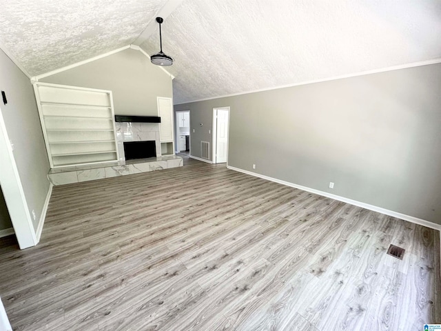 unfurnished living room featuring light wood-type flooring, lofted ceiling, a high end fireplace, and a textured ceiling