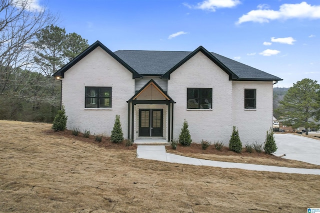 modern farmhouse style home with french doors, brick siding, and roof with shingles