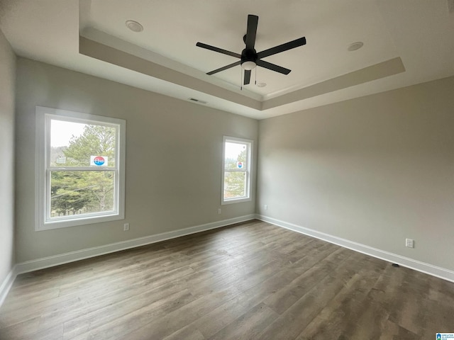 unfurnished room featuring ceiling fan, wood-type flooring, and a raised ceiling