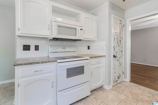 kitchen with white appliances, white cabinetry, a textured ceiling, and dark stone counters