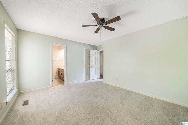 unfurnished bedroom featuring light carpet, a textured ceiling, ensuite bath, and ceiling fan