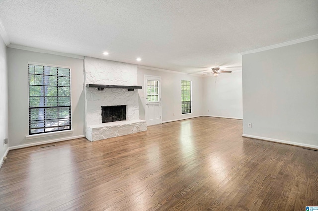 unfurnished living room featuring ceiling fan, a stone fireplace, a wealth of natural light, and dark hardwood / wood-style flooring