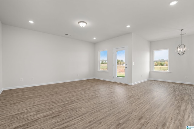 unfurnished room with plenty of natural light, wood-type flooring, and an inviting chandelier